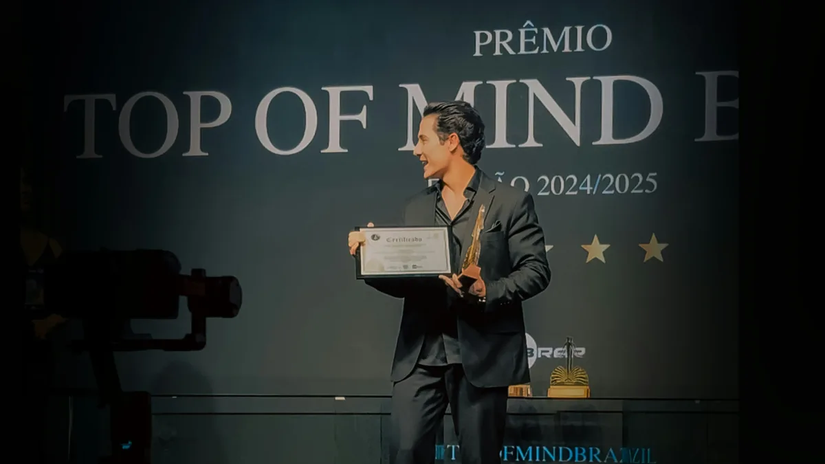 A man in a suit holding an award and standing in front of a projector screen with text on it.