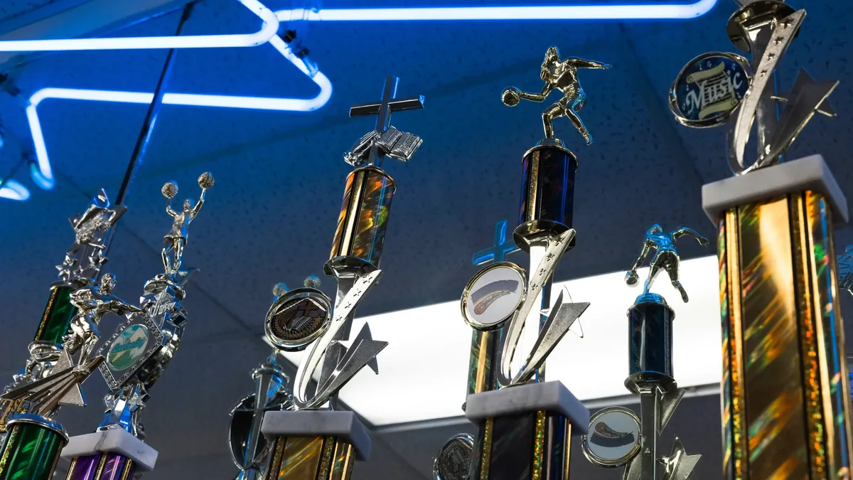 A collection of trophies on display, with a blue ceiling and white neon lights in the background.